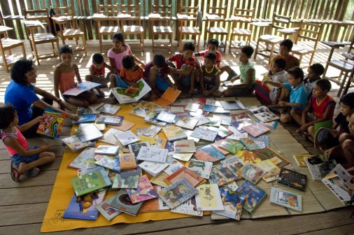 Children sitting around blanket with books in front of them